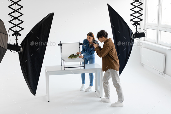 Professional team of photographer and content manager shooting stylish shoes in photostudio, working