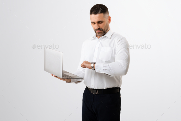 Business career and time management. Middle aged businessman using laptop and checking time, grey