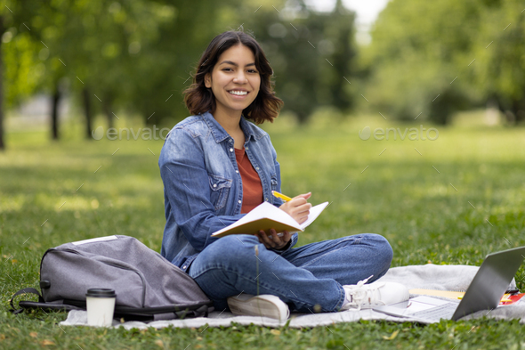 Middle Eastern Female Student Writing In Notepad While Preparing For Exam Outdoors