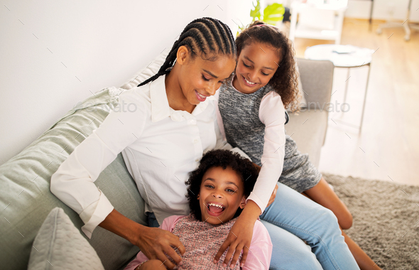 Happy Black Mom And Daughters Tickling Each Other Cuddling Indoors