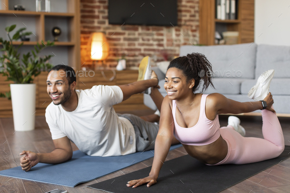 Cheerful young black family in sportswear doing leg stretching exercises on mat on floor, enjoy - Stock Photo - Images