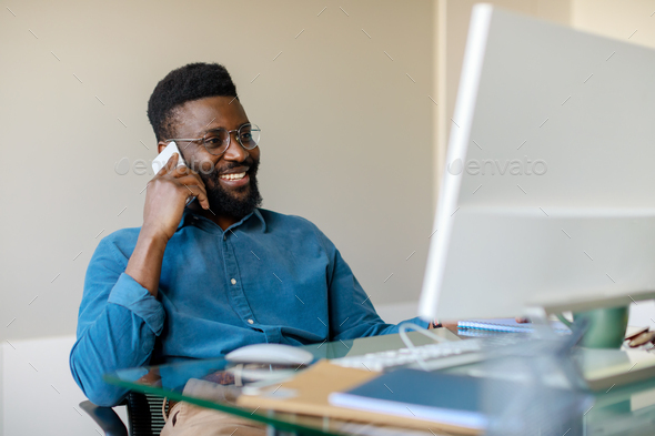 Happy black businessman having phone conversation with client, sitting in  front of computer and Stock Photo by Prostock-studio