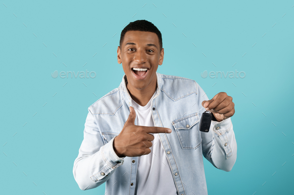 Cheerful shocked funny millennial black guy in casual pointing finger at car keys, rejoices to buy