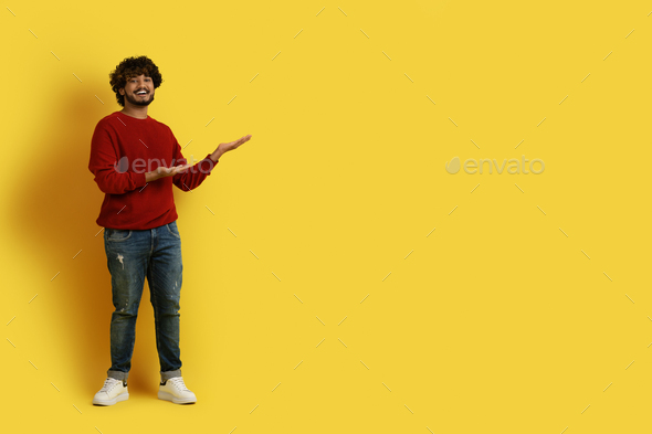 Smiling young indian guy pointing at copy space on yellow - Stock Photo - Images