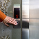 Close-up photo. The hand of a young woman in an orange shirt pressing a metal elevator button with - PhotoDune Item for Sale