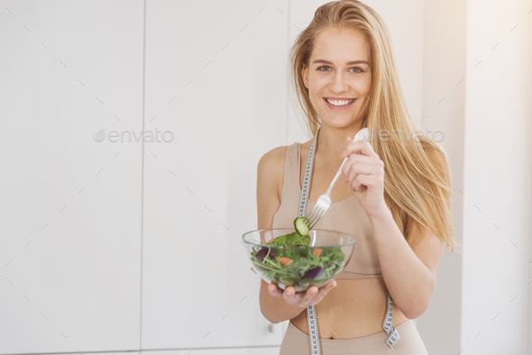 Beautiful sport girl in sportswear enjoy eat clean vegetables after exercise for health in house