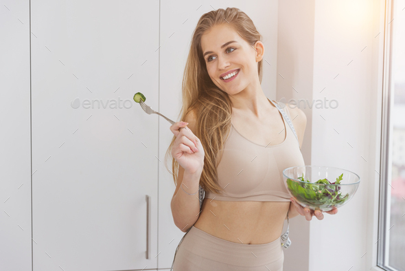 Beautiful sport girl in sportswear enjoy eat clean vegetables after exercise for health in house.