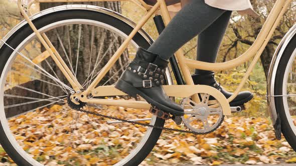Women's Legs in Fashionable Boots are Pedaling a City Bike in an Autumn Park alt