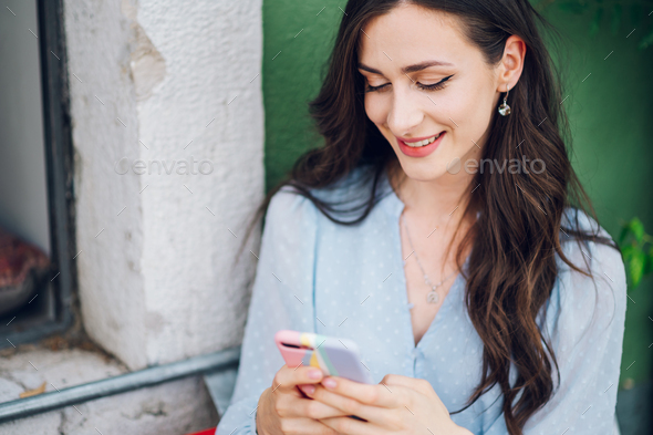 Beautiful woman sitting in a street cafe and using smartphone - Stock Photo - Images
