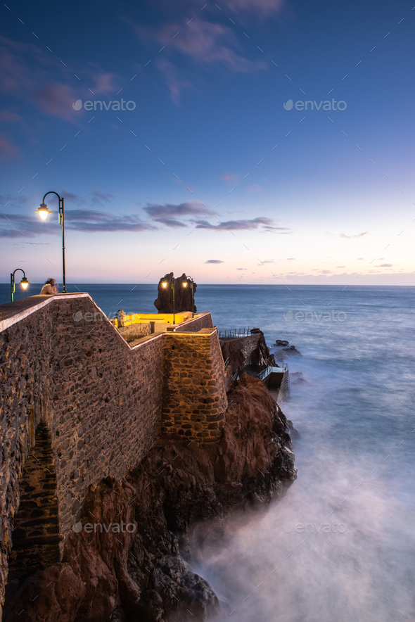 Rocks at Ponta do Sol, Madeira  beach with promenade on cliffs. Sunset light, Atlantic Ocean waves - Stock Photo - Images