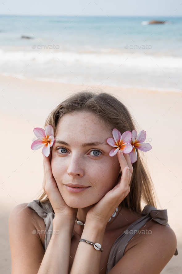 Beautiful young adult blond woman holding flowers close to face at beach - Stock Photo - Images
