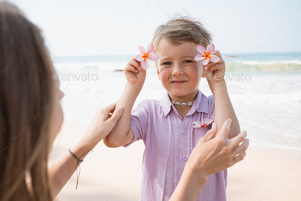 Little boy holding exotic flowers with mother at beach in sunny summer day - Stock Photo - Images