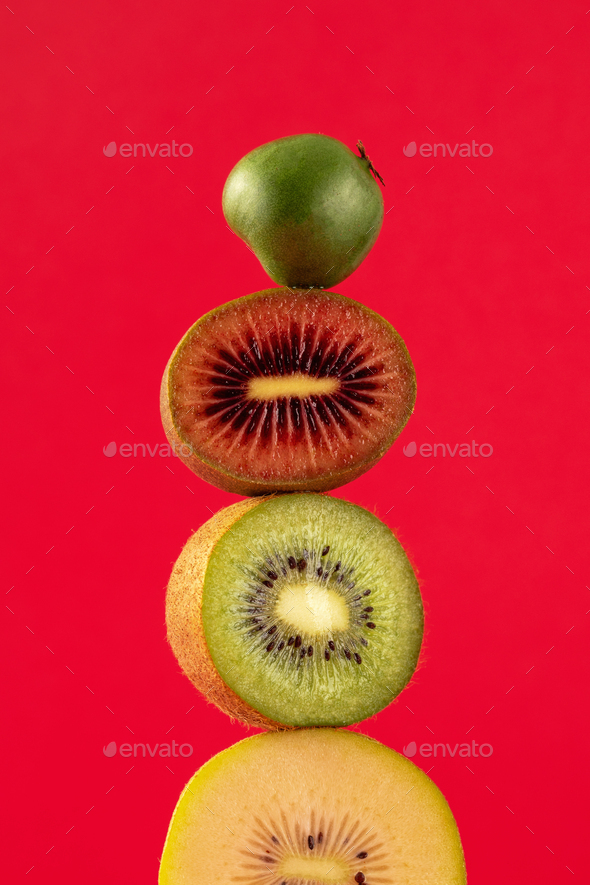 Still life with balancing kiwis of different varieties on a red. A balance of fruits, art concept. - Stock Photo - Images