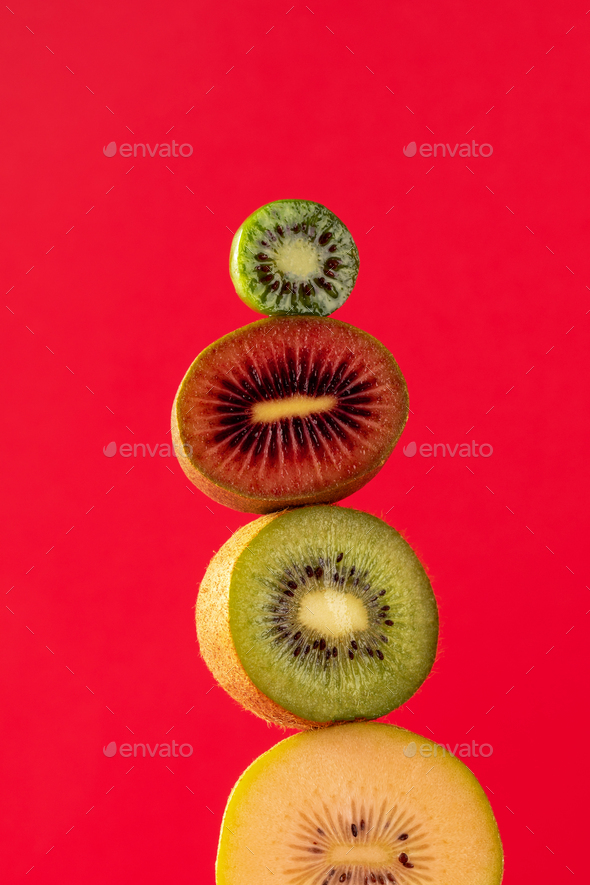 Still life with balancing kiwis of different varieties on a red. A