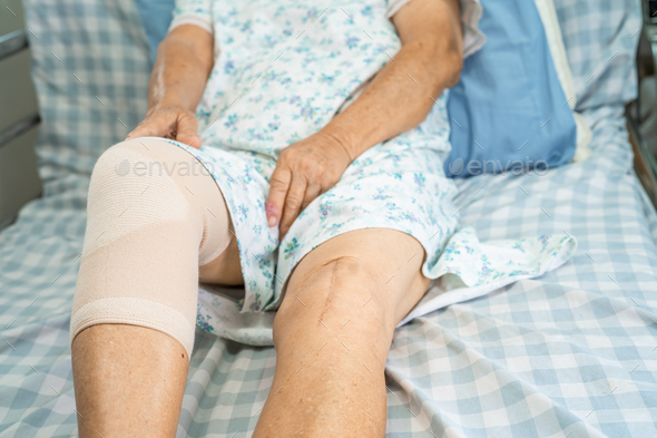 Asian elderly woman patient with knee support pain joint on bed in nursing hospital.