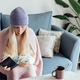 Unhappy Young woman wearing woolen hat and warm clothing at home and counting cash money. Energy - PhotoDune Item for Sale
