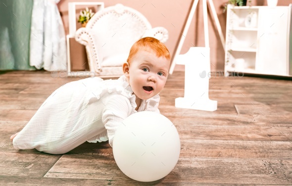 Little redhead baby girl wih balloon celebrates first birthday anniversary. 1 year family party  - Stock Photo - Images