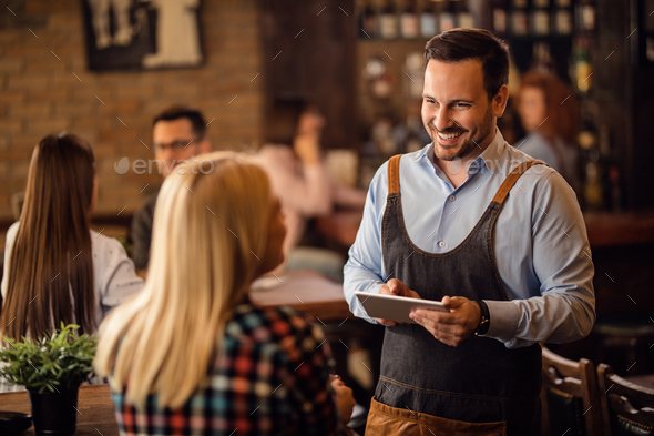 Happy waiter with touchpad taking an order from a guest in a pub.