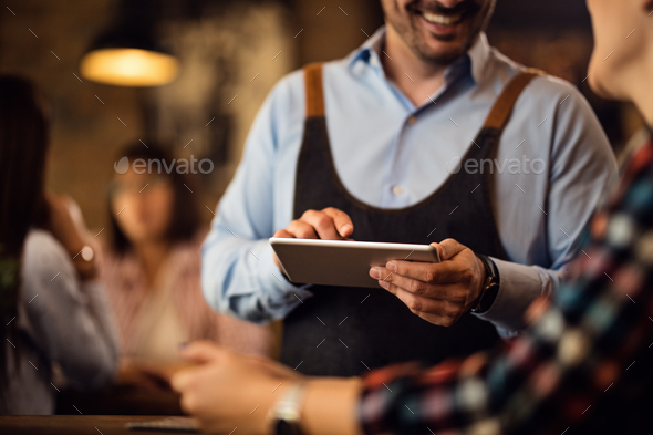 Close-up of waiter with touchpad taking order from a guest in a pub.