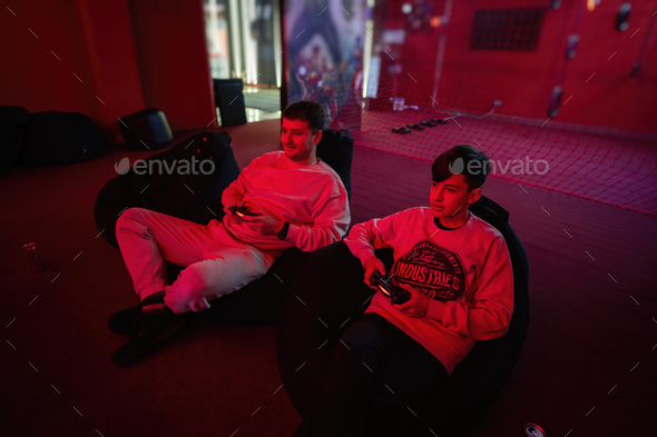 Father and son play gamepad video game console in red gaming room. Dad and kid gamers.