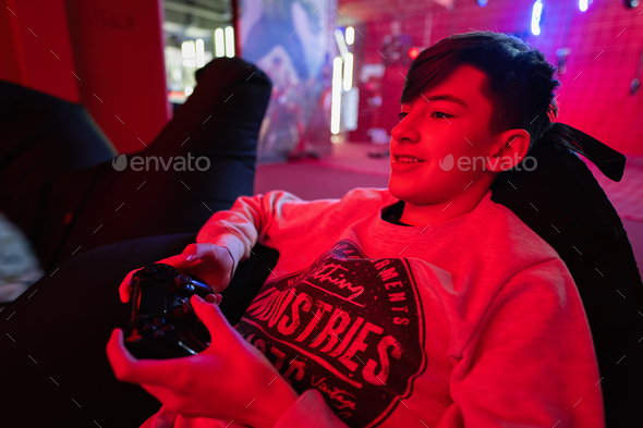 Teenager boy gamer play gamepad video game console in red gaming room.