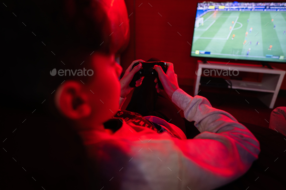Teenager boy gamer play football gamepad video game console in red gaming room.