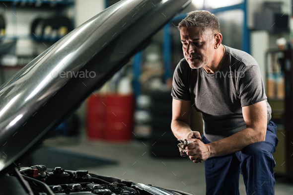 Auto mechanic wiping hands after repairing car engine in a garage.