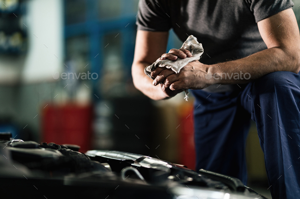 Unrecognizable auto mechanic wiping his hands in a repair shop.