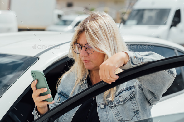 Woman standing near car and looking at her mobile phone, paying for parking.
