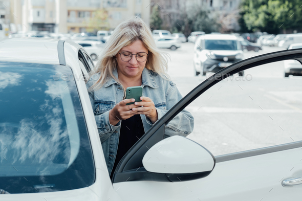 Woman standing near car and looking at her smartphone, paying for parking.