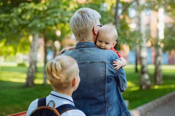 caucasian blond haired woman carry baby daughter. Schoolboy son looking at little sister - Stock Photo - Images