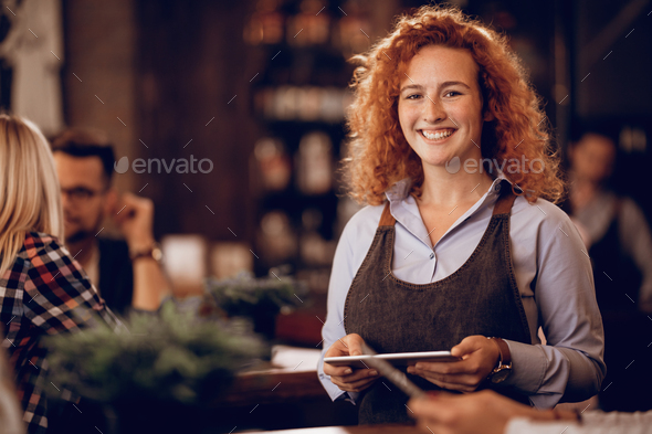 Portrait of young happy waitress with digital tablet in a bar.