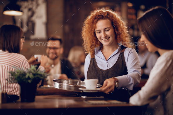 Happy waitress serving coffee to a customer in a cafe.