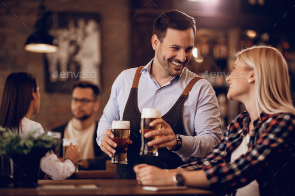 Happy waiter communicating with a guest while serving her beer in a pub. - Stock Photo - Images