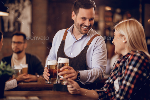 Happy waiter serving beer to female customer in a bar. - Stock Photo - Images