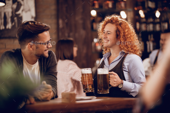 Young happy waitress serving beer to her customer in a bar. - Stock Photo - Images