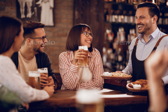 Cheerful waiter serving food to his guests in a pub. - Stock Photo - Images