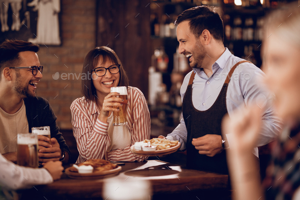 Happy waiter having fun with customers while serving them in a pub. - Stock Photo - Images