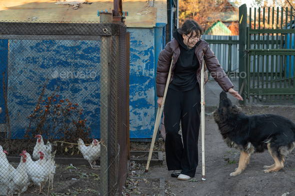 a girl on crutches walks in the yard with a dog and chickens