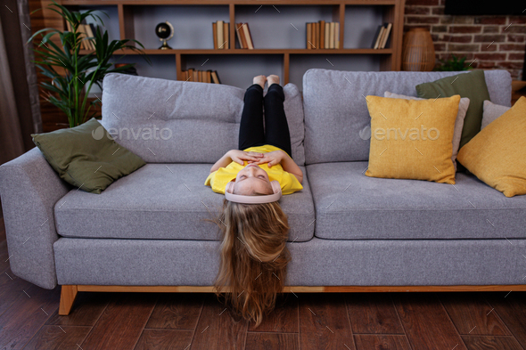Happy child listens to music or audiobook at home on couch. Little school kid wearing headphones - Stock Photo - Images