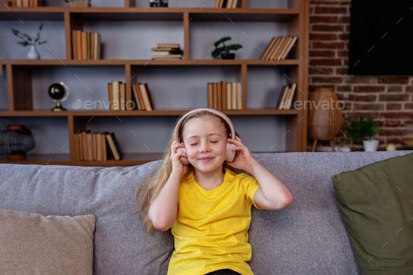 Happy child listens to music or audiobook at home on couch. Little school kid wearing headphones. - Stock Photo - Images