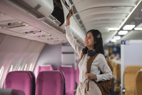 Young asian woman travel by airplane. Passenger putting hand baggage in lockers above seats of - Stock Photo - Images