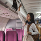 Young asian woman travel by airplane. Passenger putting hand baggage in lockers above seats of - PhotoDune Item for Sale