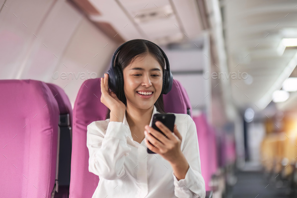 Cheerful female passenger in headphones for noise cancellation watching online movie during - Stock Photo - Images