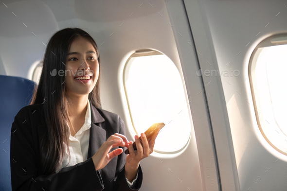 Traveling and technology. Flying at first class. Pretty young business woman using smartphone while - Stock Photo - Images