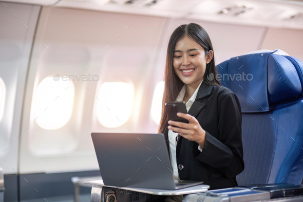 Traveling and technology. Flying at first class. Pretty young business woman using smartphone while - Stock Photo - Images