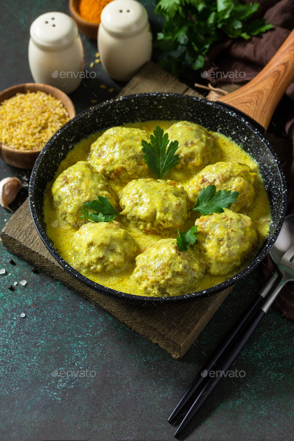 Meatballs with bulgur in sour cream and turmeric sauce in a cast-iron skillet.  - Stock Photo - Images