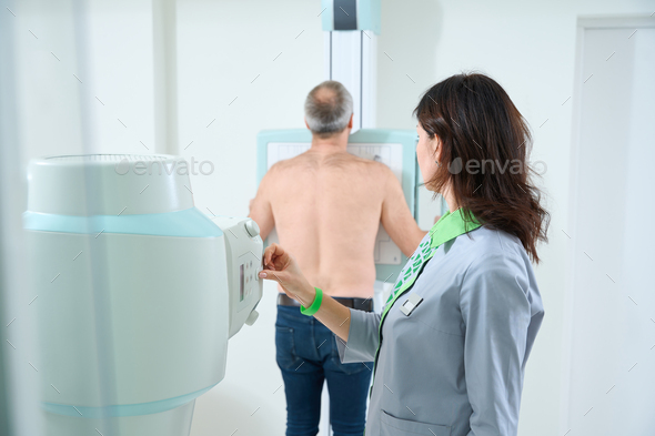 Female doctor adjusting equipment while male patient scanning chest - Stock Photo - Images