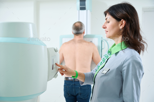 Doctor operating X-ray machine while standing near the patient - Stock Photo - Images