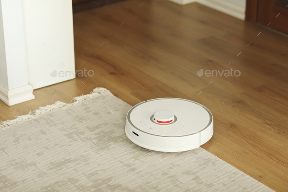 white robot vacuum cleaner cleans the floor from debris,home cleaning with an electric vacuum clean
